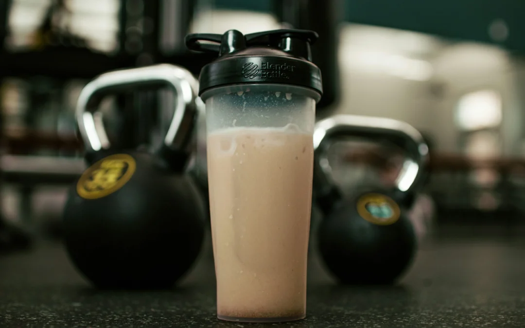 Generic protein shaker filled with protein powder shake in front of two black kettlebells in dark moody gym setting.
